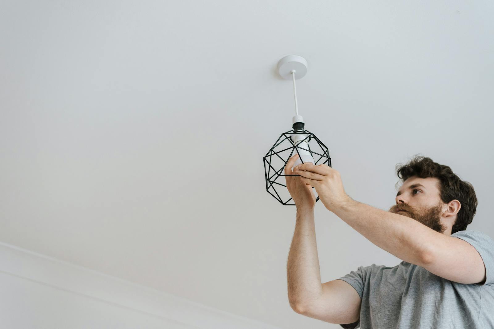 A professional electrician skillfully installing a modern geometric ceiling lamp indoors.