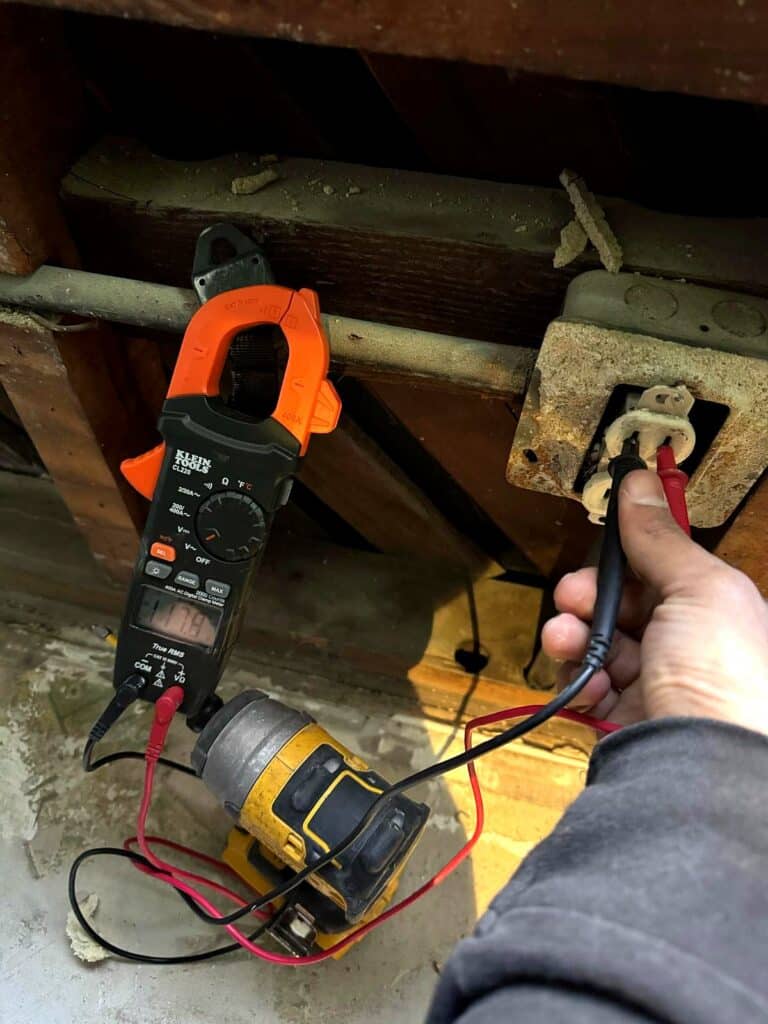 Volta Electric electrician testing an outlet in a crawl space with a clamp meter