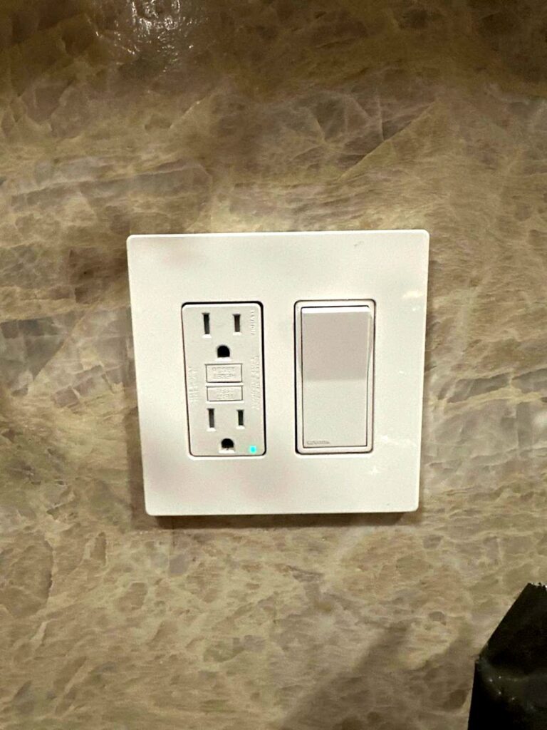GFCI outlet and light switch on a marble bathroom wall, installed by Volta Electric