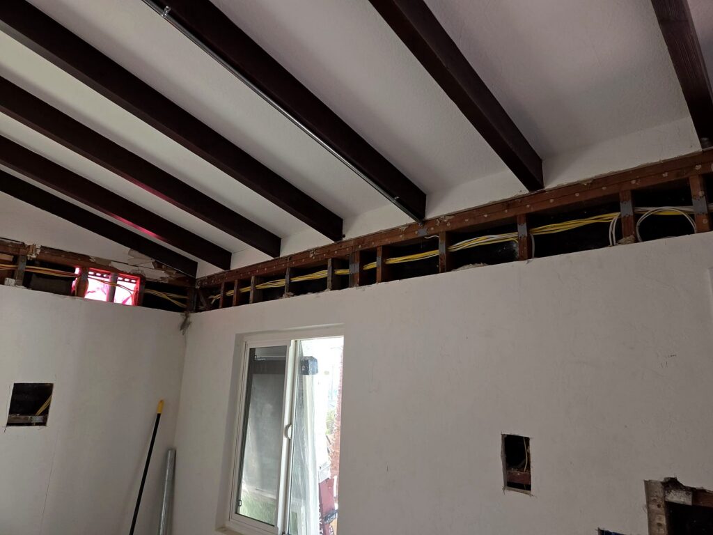 Volta Electric rewire in progress: new electrical cable run through a narrow opening along the top of the walls, under a beamed ceiling