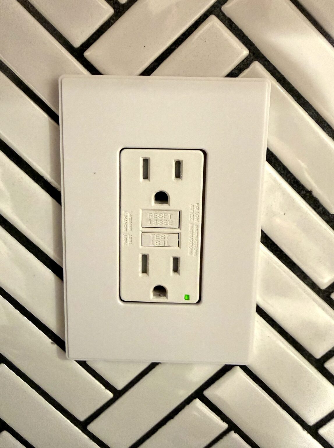 White GFCI outlet with a screwless wall plate on a herringbone tile backsplash, installed by Volta Electric