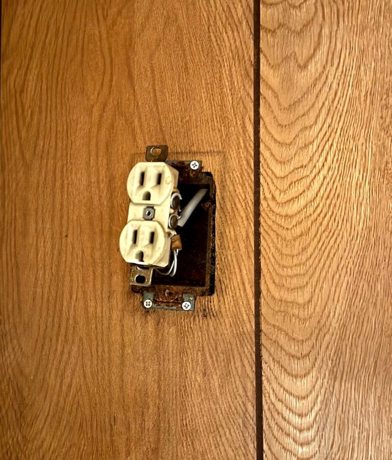 Old outlet hanging loose from a rusted wall box with exposed wiring