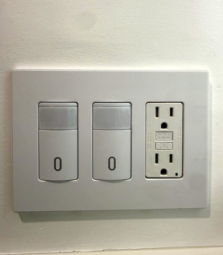 Two occupancy sensor light switches and a GFCI outlet under one screwless white wall plate