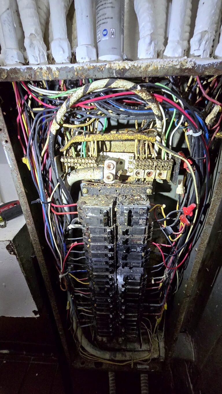 Old electrical panel with heavy corrosion and crowded, tangled wiring