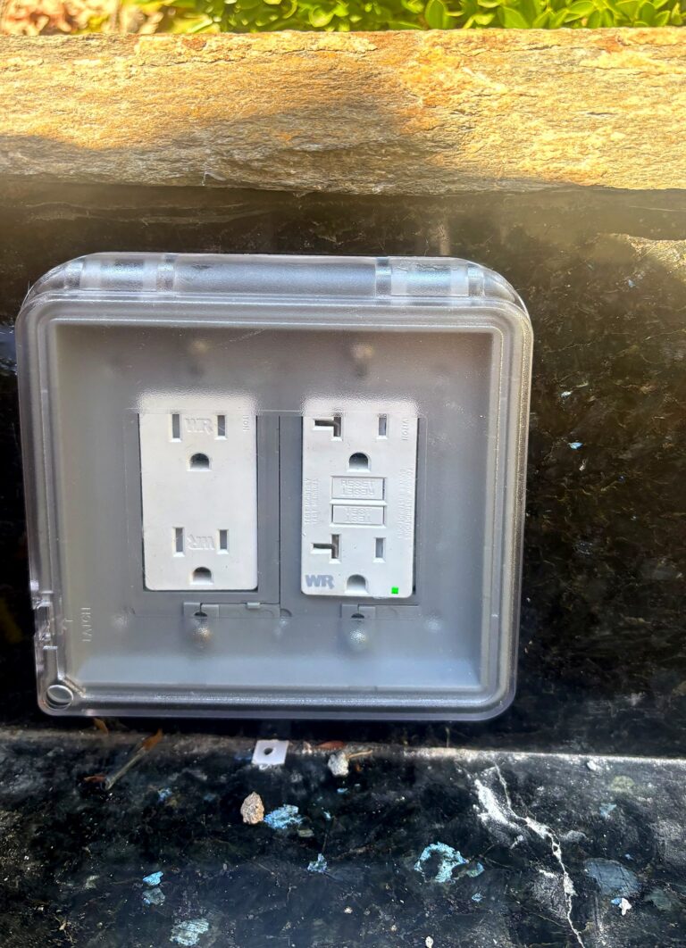 Outdoor weather-resistant GFCI outlets inside a clear in-use cover on a stone wall