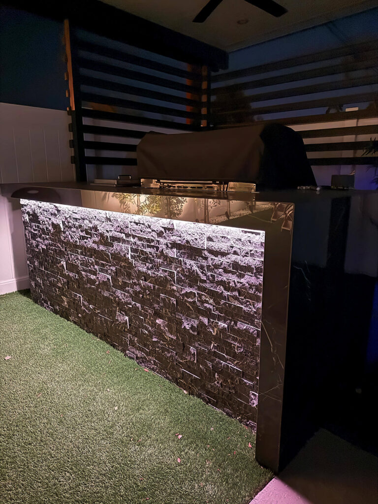 LED strip light glowing under the countertop of a stacked-stone outdoor kitchen island at night