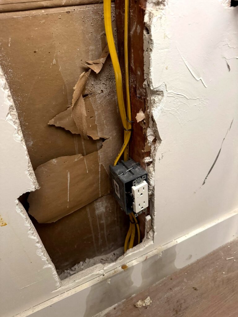Wall opened to repair outlet wiring, with a new outlet box and cable secured to the stud