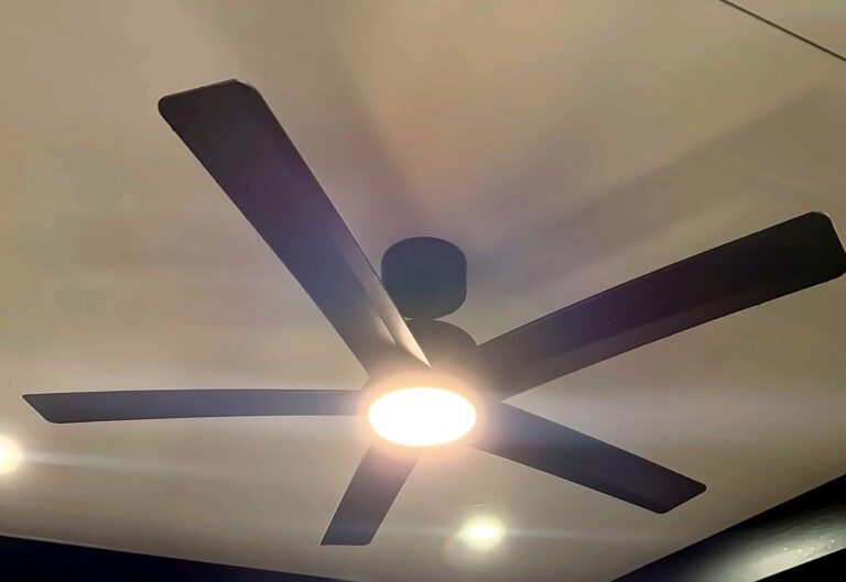 Black five-blade ceiling fan with a glowing LED light on a covered patio ceiling, with recessed lights