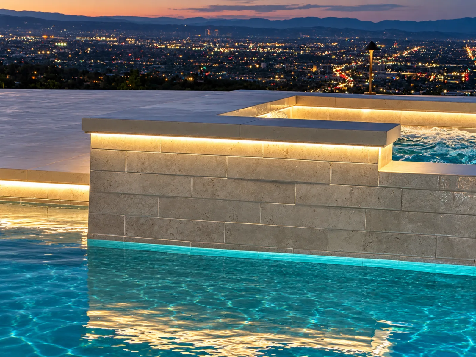 Spa and pool LED lighting installed by Volta Electric, glowing at dusk with city lights in the distance