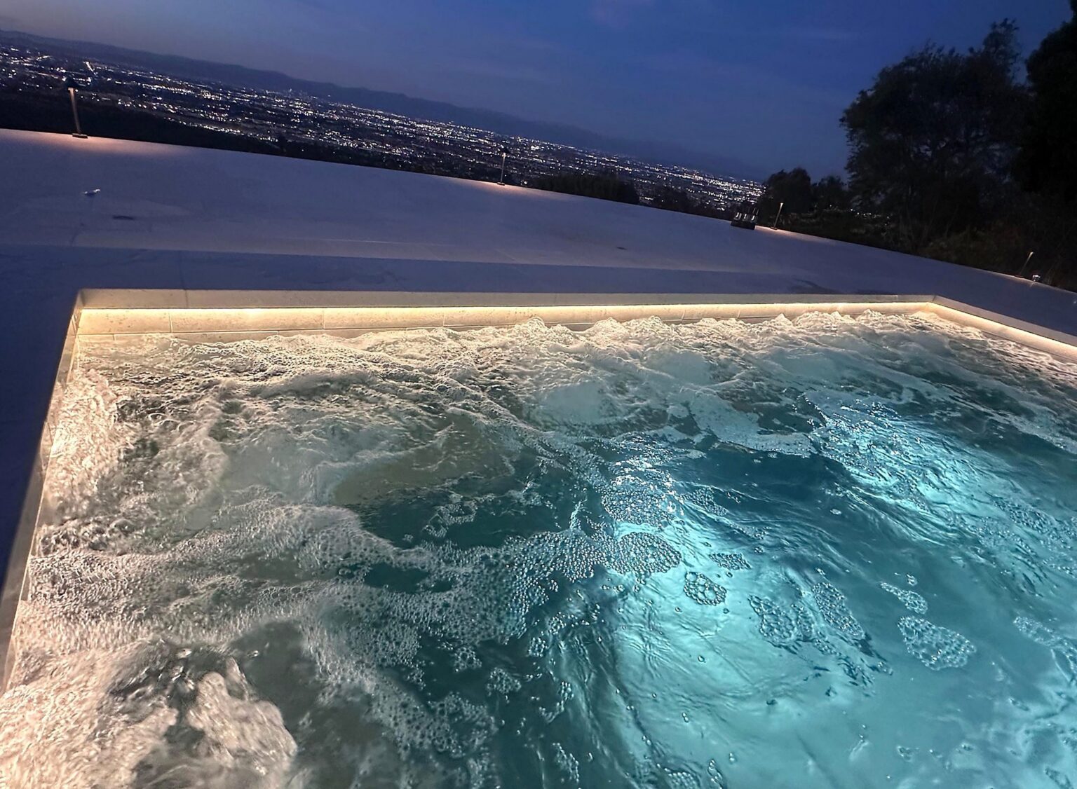 Spa with warm LED lighting along the edge at dusk, city lights in the distance, installed by Volta Electric